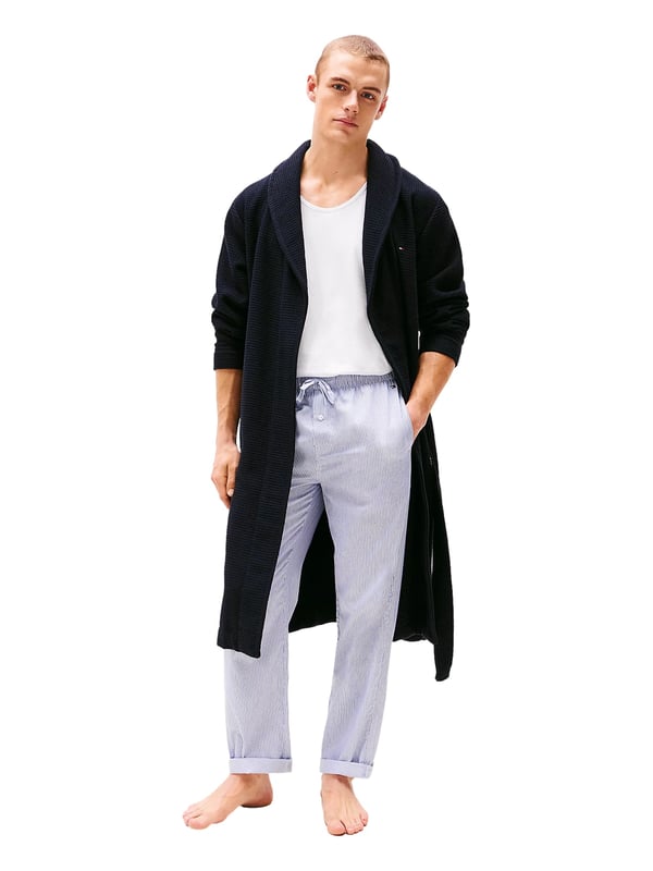 Tommy Hilfiger Bademantel Dieser Herren-Bademantel überzeugt mit stilvoller Waffelstruktur und angenehm zu tragendem Gefühl. Der klassische Schalkragen verleiht ihm eine elegante Note und lädt zum Einkuscheln ein. Mit dem Bindegürtel lässt sich die Passform individuell anpassen – ganz nach deinem Komfort. Zwei aufgesetzte Taschen vorne bieten Platz für kleine Essentials oder einfach warme Hände. Leicht überschnittene Schultern sorgen für eine entspannte Silhouette und zusätzliche Bewegungsfreiheit. Das Label-Necktape im Nackenbereich unterstreicht die hochwertige Verarbeitung. Eine dezente Logo-Stickerei auf der Brust setzt ein geschmackvolles Markenstatement. Der Stoff ist leicht, aber dennoch wärmend – ideal für gemütliche Morgen oder entspannte Abende. Ob nach der Dusche oder beim Frühstück auf dem Balkon, dieser Bademantel macht jede Auszeit noch angenehmer. Für Männer, die sich stilvoll entspannen wollen.