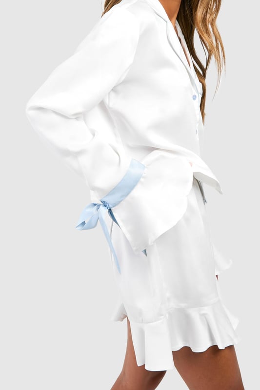 Bridal Something Blue Long Sleeve Shirt & Shorts Pyjama Set Luxurious satin pyjama set for bridal occasions
Chic short-length design for comfort and style
Elegant notched collar and button-front closure
Charming blue bow details on sleeves
Feminine ruffle hem on shorts for a playful touch
Indulge in bridal bliss with this enchanting short pyjama set from Boohoo. Perfect for your special day, this satin ensemble combines comfort with sophistication. The button-front top features a classic notched collar and long sleeves adorned with delightful blue bows, adding a touch of 'something blue' to your bridal attire. The matching shorts boast a flirty ruffle hem, creating a playful silhouette. Ideal for pre-wedding preparations, a relaxing honeymoon morning, or a stylish hen do sleepover. Pair with soft slippers and a silky robe for ultimate lounging luxury, or dress it up with elegant jewellery and a glass of bubbly for those picture-perfect getting-ready moments. This versatile set ensures you'll feel every bit the radiant bride, even in your most intimate moments.