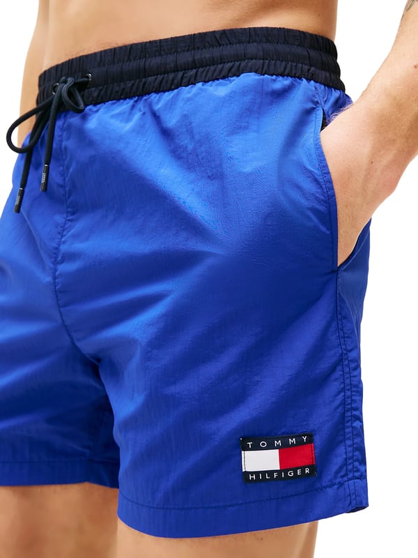 Tommy Hilfiger Schwimmshorts Diese Herren-Badeshorts im Slim Fit überzeugen mit sportlicher Eleganz und passgenauem Sitz. Der oberschenkellange Schnitt betont die Figur und bietet dennoch volle Bewegungsfreiheit. Ein farblich abgesetzter Bund mit Tunnelzug setzt einen frischen Akzent und sorgt für sicheren Halt. Seitliche Eingrifftaschen und eine Gesäßtasche bieten praktische Verstaumöglichkeiten. Der elastische Bund passt sich flexibel an – ideal für aktive Tage am Wasser. Der leichte Stoff trocknet schnell und trägt sich auch nach dem Schwimmen angenehm. Ein dezenter Label-Aufnäher am Bein rundet das Design markant ab. Diese Shorts machen am Strand ebenso eine gute Figur wie auf der Promenade. Schmal geschnitten, aber maximal bequem. Für Männer, die auf Stil auch beim Baden nicht verzichten möchten.