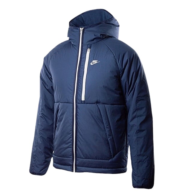 Stay warm and dry with the Nike Dark Blue Padded Jacket, crafted from 100% polyester with Therma-FIT technology to retain heat efficiently. This water-repellent jacket features a full zip fastening for easy wear, two front pockets secured with buttons, and a zippered left breast pocket for secure storage. The attached hood offers extra protection against the elements, while the iconic Nike badge on the left breast adds a stylish touch. Perfect for outdoor activities or casual wear, this jacket combines functionality and comfort in a sleek design