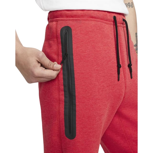 Nike - Schwarze Jogginghose Mit Verschweißten Reißverschlüssen Und Rot Erleben Sie Komfort und Style mit der Nike Black Taped Zips Red Sweatpants. Sie besteht aus einem weichen Materialmix aus 53 % Baumwolle und 47 % Polyester für Strapazierfähigkeit und Atmungsaktivität. Der elastische Bund und die Bündchen sowie der Kordelzug sorgen für einen sicheren, verstellbaren Sitz. Die Slim-Fit-Jogginghose mit schmal zulaufendem Bein und regulärer Länge bietet eine moderne Silhouette. Zu den praktischen Details gehören zwei Fronttaschen, eine davon mit Reißverschluss zur sicheren Aufbewahrung wichtiger Utensilien, und das ikonische Nike Swoosh-Logo auf der linken Hüfte verleiht ihr einen sportlichen Touch. Diese Jogginghose ist perfekt für Freizeit und Training und vereint Funktionalität mit elegantem Design