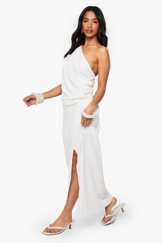Striking one-shoulder design with elegant draping detail
        Flowing maxi length with side split for effortless movement
        Dramatic open back feature adds a sultry touch
        Linen-look fabric offers a lightweight, textured finish
        Petite fit designed specifically for smaller frames
    
    This captivating draped maxi dress combines Grecian-inspired elegance with contemporary flair. The asymmetric one-shoulder neckline creates a striking silhouette, while the flowing fabric cascades beautifully to the floor with a side split that allows for graceful movement. Perfect for evening soires, pair with strappy heels and statement bangles as shown for a sophisticated nightlife look. The open back detail adds an unexpected twist to this otherwise classic design. Versatile enough for upscale cocktail events or summer parties, this dress can be styled with metallic accessories for glamorous occasions or dressed down with flat sandals for more casual gatherings. The linen-look texture adds dimension and interest to this Boohoo showstopper that's sure to turn heads on your next night out.
