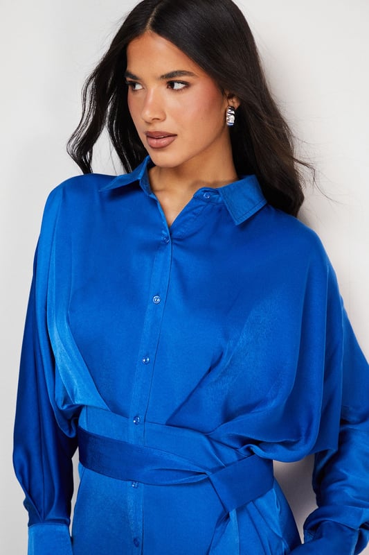 Striking batwing sleeves for a dramatic silhouette
        Elegant midi length with a daring side split
        Collared neckline adds a touch of sophistication
        Button-down front for versatile styling options
        Cinched waist design creates a flattering shape
    
    This satin shirt dress from Warehouse is a versatile piece that effortlessly transitions from day to night. The batwing sleeves create a bold, contemporary look, while the midi length with a side split adds a hint of allure. Perfect for confident women who appreciate edgy yet feminine styles, this dress can be styled for various casual occasions. For a chic daytime ensemble, pair it with ankle boots and a crossbody bag for a family lunch or weekend outing. Layer with a leather jacket for an edgier look when meeting friends for coffee. The button-down front allows for customisable coverage, making it suitable for different settings. Accessorise with statement earrings and a sleek updo for an evening dinner date. The dress's fluid silhouette and rich texture make it a standout piece in any wardrobe, ideal for those who want to make a subtle yet impactful fashion statement.