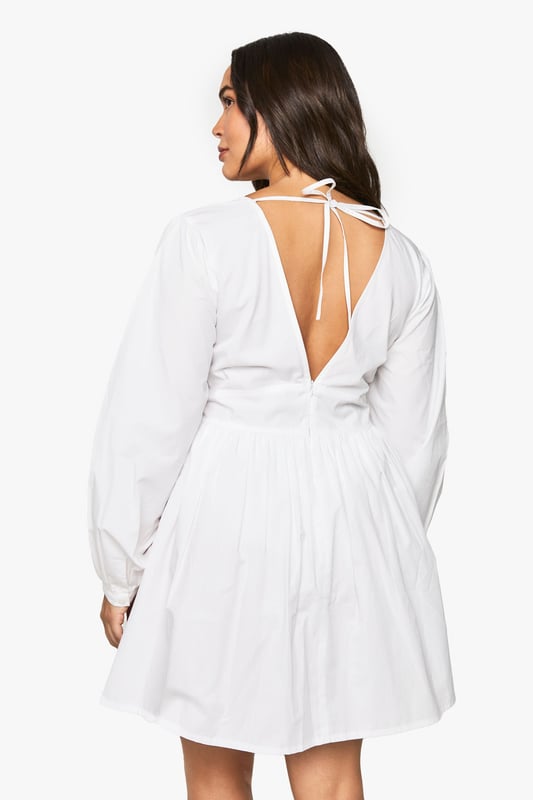 Flattering V-neckline with smocked bodice detail for a comfortable fit
        Voluminous blouson sleeves that create a romantic silhouette
        Open back design with delicate tie fastening for an unexpected twist
        Relaxed A-line shape with gathered skirt for effortless movement
        Versatile mini length perfect for day-to-night styling
    
    This charming cotton smock dress combines comfort with contemporary style. The smocked bodice creates a flattering fit whilst the blouson sleeves add a touch of drama to this otherwise understated piece. The open back with tie detail offers a playful element that's perfect for warmer days. Style with white trainers and a mini handbag for casual daytime outings, as shown on our model. For family gatherings or brunch dates, pair with delicate jewellery and strappy sandals. The relaxed silhouette makes this Boohoo dress a versatile addition to your wardrobe that works beautifully for garden parties, weekend shopping trips, or casual meet-ups with friends. The easy-to-wear design ensures you'll reach for this dress time and again throughout the seasons.