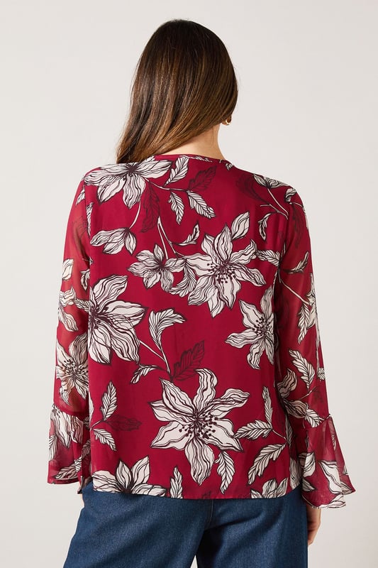Elegant V-neckline with cascading ruffle detail for a feminine touch
        Striking floral print throughout for a sophisticated daytime look
        Graceful bell sleeves with flared cuffs adding movement and charm
        Lightweight woven fabric offering comfort and easy wearability
        Versatile silhouette that can be styled tucked in or worn loose
    
    This Wallis blouse combines sophistication with effortless style through its beautiful ruffle detailing and eye-catching floral pattern. The flattering V-neckline frames the dcolletage beautifully, while the statement bell sleeves create a graceful silhouette that moves with you. Perfect for daytime occasions, style this versatile piece with wide-leg denim trousers as shown for a casual family lunch, or tuck into a tailored skirt for garden parties. The lightweight fabric ensures all-day comfort without compromising on style. Accessorise with simple gold-toned jewellery and a slouchy tote bag for a complete look that transitions seamlessly from shopping trips to casual gatherings. This blouse offers the glamour and sophistication Wallis is known for while maintaining practicality for everyday wear.
