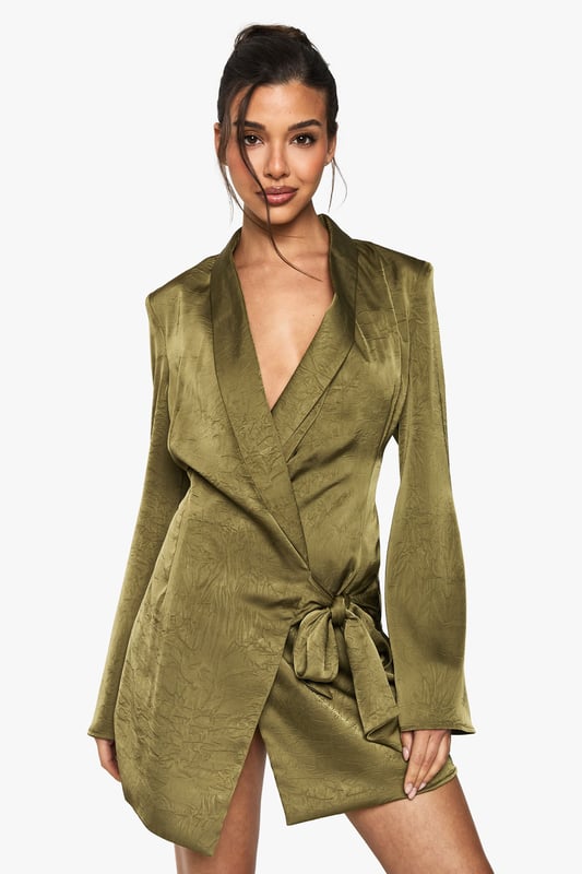 Striking wrap-style blazer dress with a daring plunge neckline
        Luxurious satin fabric with distinctive crinkle texture for added dimension
        Elegant side tie detail creates a flattering silhouette
        Statement long sleeves with subtle flared cuffs
        Structured shoulders and lapel detailing for a sophisticated tailored look
    
    Make an unforgettable entrance in this show-stopping wrap blazer dress from Boohoo. The lustrous satin fabric catches the light beautifully whilst the crinkle texture adds contemporary flair to this evening essential. The plunging neckline creates a bold statement, perfectly balanced by the sophisticated blazer-inspired design. Style with strappy heels and statement earrings as seen on our model for a night out in the city. The side tie cinches the waist for a figure-enhancing effect, whilst the mini length showcases your legs to perfection. This versatile piece transitions effortlessly from cocktails with the girls to dancing until dawn. Complete your look with a sleek updo and a compact clutch bag to let this head-turning dress command all the attention.
