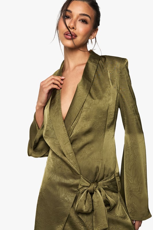 Striking wrap-style blazer dress with a daring plunge neckline
        Luxurious satin fabric with distinctive crinkle texture for added dimension
        Elegant side tie detail creates a flattering silhouette
        Statement long sleeves with subtle flared cuffs
        Structured shoulders and lapel detailing for a sophisticated tailored look
    
    Make an unforgettable entrance in this show-stopping wrap blazer dress from Boohoo. The lustrous satin fabric catches the light beautifully whilst the crinkle texture adds contemporary flair to this evening essential. The plunging neckline creates a bold statement, perfectly balanced by the sophisticated blazer-inspired design. Style with strappy heels and statement earrings as seen on our model for a night out in the city. The side tie cinches the waist for a figure-enhancing effect, whilst the mini length showcases your legs to perfection. This versatile piece transitions effortlessly from cocktails with the girls to dancing until dawn. Complete your look with a sleek updo and a compact clutch bag to let this head-turning dress command all the attention.