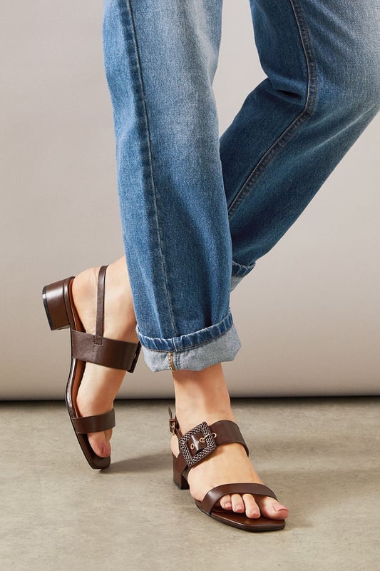 Stylish slingback design with adjustable buckle fastening for a secure fit
        Distinctive raffia-textured buckle detail adds a touch of artisanal flair
        Comfortable low block heel measuring between 2.5-4.5cm for all-day wearability
        Clean-lined silhouette with minimalist strap detailing for versatile styling
        Faux leather construction offers a sophisticated finish with practical durability
    
    The Raelynn sandals from Wallis present the perfect balance of comfort and sophistication for your daytime wardrobe. The thoughtfully designed low block heel provides stability whilst the slingback style with its distinctive raffia buckle detail adds a touch of textural interest to any ensemble. These versatile sandals pair beautifully with flowing midi dresses as shown, but work equally well with tailored trousers or casual denim. Ideal for garden parties, weekend brunches or casual family gatherings where you want to look polished without sacrificing comfort. The neutral tone makes these an excellent investment piece that will complement numerous outfits throughout the warmer months. For a coordinated daytime look, match with a structured handbag and delicate jewellery to showcase your sophisticated yet relaxed style.