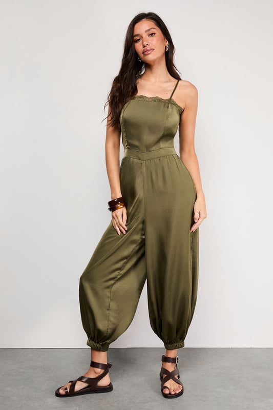 Delicate lace trim along the neckline adds a feminine touch to this satin jumpsuit
        Adjustable strappy design ensures a comfortable, personalised fit
        Elasticated cuffs create a distinctive balloon silhouette for the legs
        Relaxed fit through the body offers effortless movement and comfort
        Petite sizing ensures the perfect proportions for smaller frames
    
    This Warehouse satin jumpsuit combines casual comfort with sophisticated style. The lustrous fabric catches the light beautifully whilst the elasticated cuffs create a fashionable balloon silhouette that's both on-trend and flattering. Perfect for daytime gatherings, style with flat strappy sandals and wooden bangles for a relaxed garden party or family lunch. For cooler evenings, layer with an oversized denim jacket and switch to ankle boots. The versatile design transitions seamlessly from casual brunches to evening drinks - simply add statement earrings and a clutch bag to transform your look. The adjustable straps allow you to customise the fit, making this jumpsuit a wardrobe essential that works hard for your everyday style.