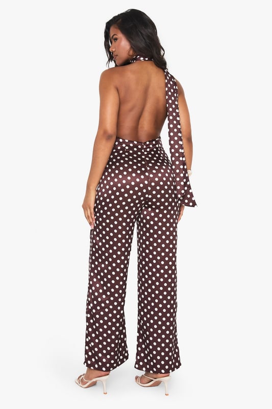 Striking polka dot satin jumpsuit with elegant high neck design
        Sophisticated scarf detail adds dramatic flair to the neckline
        Flattering wide-leg silhouette for effortless movement
        Statement open back design for head-turning appeal
        Perfect one-piece solution for special occasions with minimal styling required
    
    Make a striking entrance at your next formal event in this captivating polka dot satin jumpsuit from Boohoo. The distinctive high neck with scarf detail creates a sophisticated focal point, while the open back adds a touch of allure. The wide-leg cut offers both comfort and elegance, creating a flowing silhouette that moves beautifully as you walk. Style with metallic strappy heels as shown for a refined evening look, and add statement earrings to complement the neckline. This versatile piece transitions seamlessly from weddings to graduation ceremonies and race day events. For cooler evenings, layer with a tailored blazer or delicate wrap to maintain the jumpsuit's elegant profile whilst adding warmth.