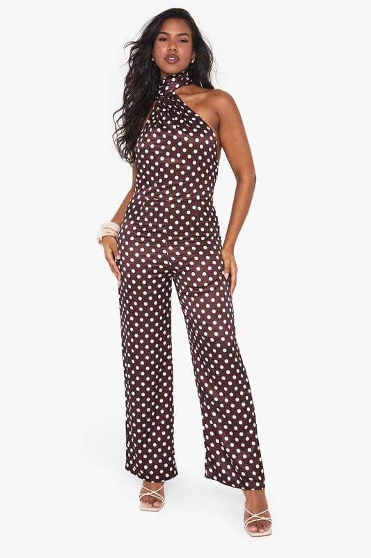 Striking polka dot satin jumpsuit with elegant high neck design
        Sophisticated scarf detail adds dramatic flair to the neckline
        Flattering wide-leg silhouette for effortless movement
        Statement open back design for head-turning appeal
        Perfect one-piece solution for special occasions with minimal styling required
    
    Make a striking entrance at your next formal event in this captivating polka dot satin jumpsuit from Boohoo. The distinctive high neck with scarf detail creates a sophisticated focal point, while the open back adds a touch of allure. The wide-leg cut offers both comfort and elegance, creating a flowing silhouette that moves beautifully as you walk. Style with metallic strappy heels as shown for a refined evening look, and add statement earrings to complement the neckline. This versatile piece transitions seamlessly from weddings to graduation ceremonies and race day events. For cooler evenings, layer with a tailored blazer or delicate wrap to maintain the jumpsuit's elegant profile whilst adding warmth.