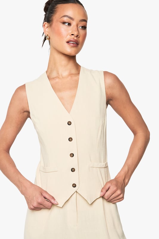 Sleeveless waistcoat with linen-look texture for a relaxed yet refined aesthetic
        V-neckline and button-through front with contrasting buttons for added visual interest
        Tailored fit designed specifically for taller frames, offering proper proportions
        Practical front pockets perfect for small essentials or a casual hand placement
        Versatile layering piece that transitions effortlessly between seasons
    
    This linen-look waistcoat brings a touch of understated sophistication to your wardrobe. Designed with the taller frame in mind, it offers the perfect proportions for a flattering silhouette. Style it as seen with relaxed denim jeans for an effortlessly cool daytime look, or pair with tailored trousers and a crisp shirt for more formal occasions. The neutral tone makes it incredibly versatile - layer under a blazer during cooler months or wear alone with statement jewellery when temperatures rise. Perfect for family gatherings, casual office environments, or weekend brunches, this Boohoo waistcoat can be customised to suit your personal style. The textured fabric adds dimension to any outfit whilst maintaining a comfortable, breathable feel that's ideal for all-day wear.