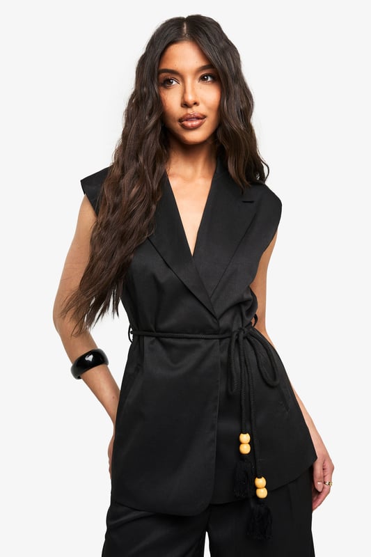 Sleeveless wrap waistcoat with sophisticated lapel detailing
        Flattering loose fit design for effortless movement
        Stylish belt with decorative wooden bead accents
        Linen-look texture adding dimension to your outfit
        Versatile layering piece suitable for multiple seasons
    
    This chic waistcoat combines contemporary styling with timeless appeal. The wrap design creates a flattering silhouette while the loose fit ensures comfort for all-day wear. Style with the coordinating wide-leg trousers as seen on our model for a polished co-ord look that's perfect for casual gatherings. For daytime outings, pair with your favourite denim and trainers, adding statement sunglasses for a touch of glamour. When evening approaches, transform your look by layering over a fitted top and accessorising with a structured handbag. The belt with wooden bead detailing adds a distinctive finishing touch that draws the eye and defines the waist. This versatile piece transitions seamlessly from family brunches to casual meetups, embodying boohoo's commitment to inclusive, trend-focused fashion that works for every occasion.