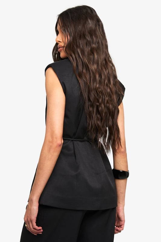 Sleeveless wrap waistcoat with sophisticated lapel detailing
        Flattering loose fit design for effortless movement
        Stylish belt with decorative wooden bead accents
        Linen-look texture adding dimension to your outfit
        Versatile layering piece suitable for multiple seasons
    
    This chic waistcoat combines contemporary styling with timeless appeal. The wrap design creates a flattering silhouette while the loose fit ensures comfort for all-day wear. Style with the coordinating wide-leg trousers as seen on our model for a polished co-ord look that's perfect for casual gatherings. For daytime outings, pair with your favourite denim and trainers, adding statement sunglasses for a touch of glamour. When evening approaches, transform your look by layering over a fitted top and accessorising with a structured handbag. The belt with wooden bead detailing adds a distinctive finishing touch that draws the eye and defines the waist. This versatile piece transitions seamlessly from family brunches to casual meetups, embodying boohoo's commitment to inclusive, trend-focused fashion that works for every occasion.