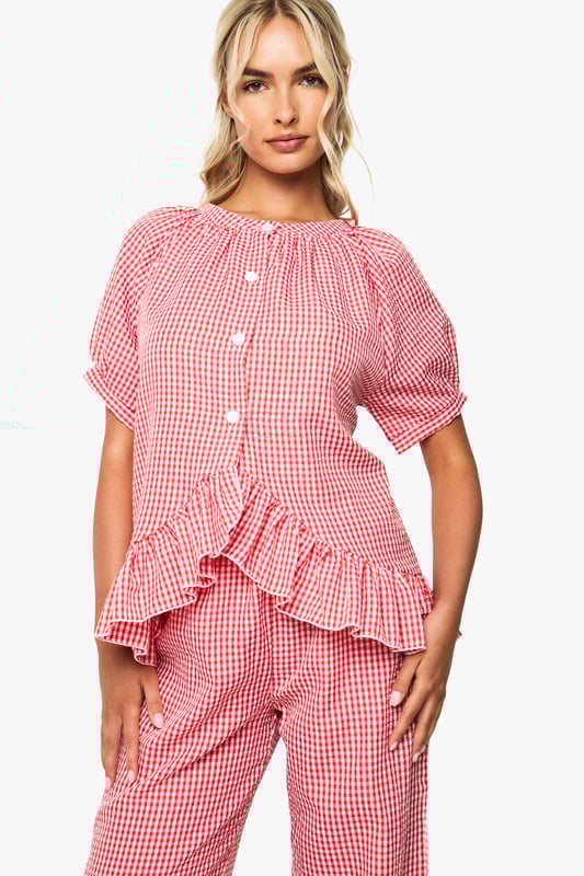 Oversized fit shirt with charming gingham pattern throughout
        Playful frill detail trim adds a feminine touch to the design
        Button-through front for easy wear and styling versatility
        Short sleeves with gentle gathering for a relaxed silhouette
        Wide-leg trousers with comfortable waistband for unrestricted movement
    
    Transform your nightwear collection with this delightfully charming gingham pyjama set from Boohoo. The oversized shirt features a gathered neckline and sweet frill detailing that adds a touch of playfulness to your evening routine. The relaxed short sleeves and button-through design ensure comfort without compromising on style. Paired with the matching wide-leg trousers, this set offers the perfect balance of comfort and fashion-forward design. Ideal for lounging at home on lazy weekend mornings or settling in for a cosy night of films and snacks. Complete your nighttime ensemble with fluffy slippers and a warm dressing gown during colder months, or wear the pieces separately to mix and match with your existing nightwear collection for versatile styling options throughout the seasons.