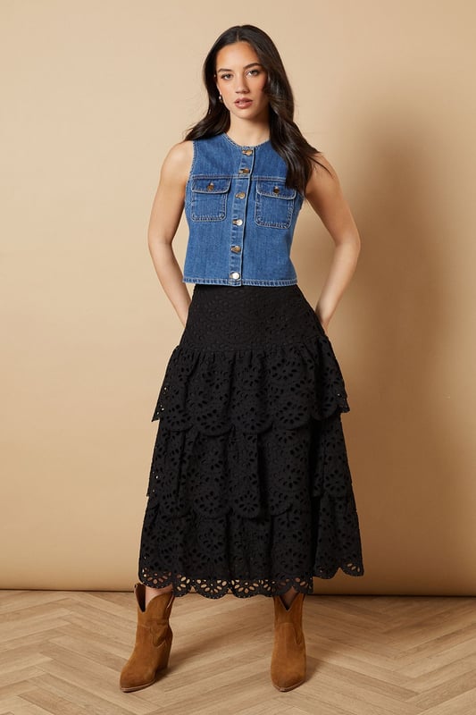 Intricate broderie anglaise detailing with floral eyelet pattern throughout
        Elegant tiered design creates beautiful movement and dimension
        Midi length falls gracefully below the knee for a feminine silhouette
        Scalloped hem adds a delicate finishing touch to each tier
        High-waisted fit accentuates the natural waistline
    
    This charming broderie tiered midi skirt from Oasis combines timeless femininity with contemporary styling. The delicate eyelet pattern creates a romantic texture that catches the light beautifully as you move, while the tiered construction adds playful volume and flow. Style with a denim waistcoat as shown for a balanced casual look, or pair with a fitted blouse for garden parties and family gatherings. The versatile midi length works wonderfully with both ankle boots for cooler days or flat sandals when the temperature rises. This skirt transitions effortlessly from daytime outings to casual evening events - simply switch your accessories to refresh your look. The high-waisted design flatters your figure whilst providing comfort for all-day wear.