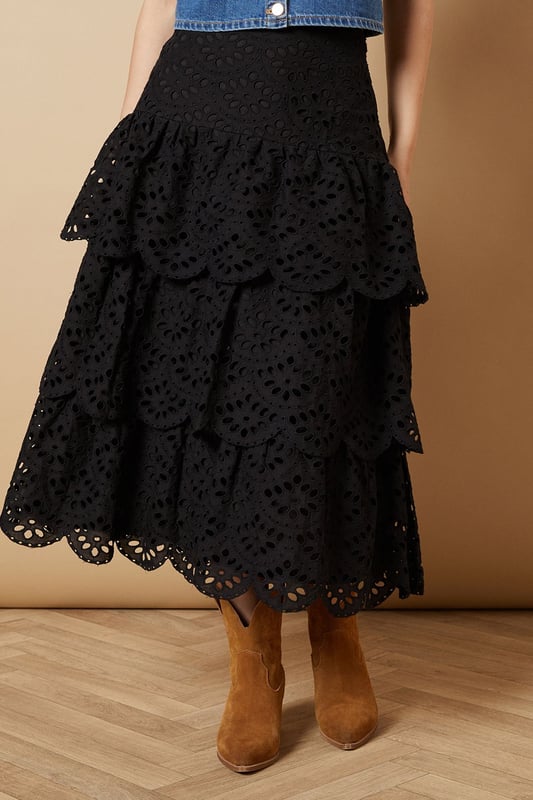 Intricate broderie anglaise detailing with floral eyelet pattern throughout
        Elegant tiered design creates beautiful movement and dimension
        Midi length falls gracefully below the knee for a feminine silhouette
        Scalloped hem adds a delicate finishing touch to each tier
        High-waisted fit accentuates the natural waistline
    
    This charming broderie tiered midi skirt from Oasis combines timeless femininity with contemporary styling. The delicate eyelet pattern creates a romantic texture that catches the light beautifully as you move, while the tiered construction adds playful volume and flow. Style with a denim waistcoat as shown for a balanced casual look, or pair with a fitted blouse for garden parties and family gatherings. The versatile midi length works wonderfully with both ankle boots for cooler days or flat sandals when the temperature rises. This skirt transitions effortlessly from daytime outings to casual evening events - simply switch your accessories to refresh your look. The high-waisted design flatters your figure whilst providing comfort for all-day wear.