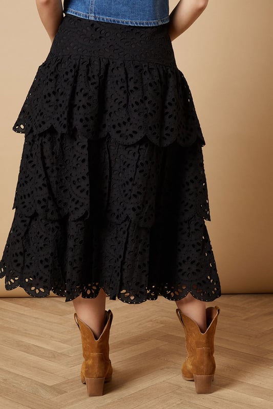 Intricate broderie anglaise detailing with floral eyelet pattern throughout
        Elegant tiered design creates beautiful movement and dimension
        Midi length falls gracefully below the knee for a feminine silhouette
        Scalloped hem adds a delicate finishing touch to each tier
        High-waisted fit accentuates the natural waistline
    
    This charming broderie tiered midi skirt from Oasis combines timeless femininity with contemporary styling. The delicate eyelet pattern creates a romantic texture that catches the light beautifully as you move, while the tiered construction adds playful volume and flow. Style with a denim waistcoat as shown for a balanced casual look, or pair with a fitted blouse for garden parties and family gatherings. The versatile midi length works wonderfully with both ankle boots for cooler days or flat sandals when the temperature rises. This skirt transitions effortlessly from daytime outings to casual evening events - simply switch your accessories to refresh your look. The high-waisted design flatters your figure whilst providing comfort for all-day wear.