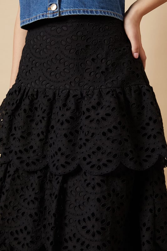 Intricate broderie anglaise detailing with floral eyelet pattern throughout
        Elegant tiered design creates beautiful movement and dimension
        Midi length falls gracefully below the knee for a feminine silhouette
        Scalloped hem adds a delicate finishing touch to each tier
        High-waisted fit accentuates the natural waistline
    
    This charming broderie tiered midi skirt from Oasis combines timeless femininity with contemporary styling. The delicate eyelet pattern creates a romantic texture that catches the light beautifully as you move, while the tiered construction adds playful volume and flow. Style with a denim waistcoat as shown for a balanced casual look, or pair with a fitted blouse for garden parties and family gatherings. The versatile midi length works wonderfully with both ankle boots for cooler days or flat sandals when the temperature rises. This skirt transitions effortlessly from daytime outings to casual evening events - simply switch your accessories to refresh your look. The high-waisted design flatters your figure whilst providing comfort for all-day wear.
