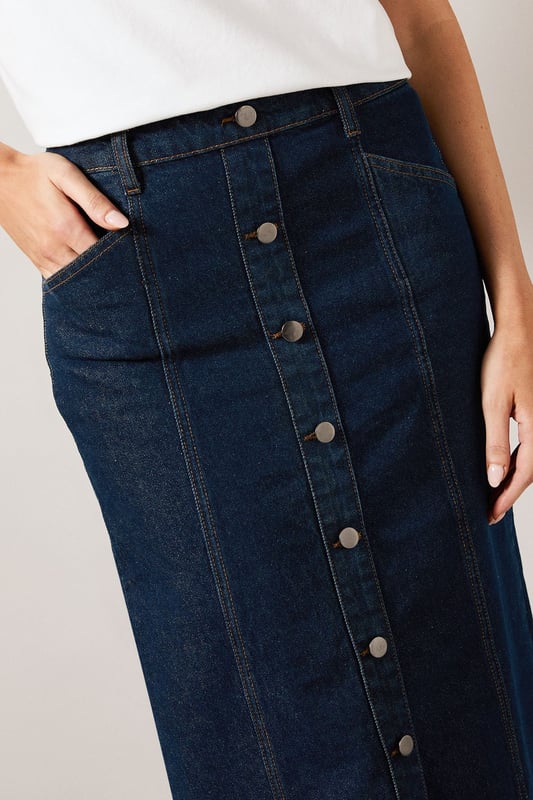 Striking midaxi length denim skirt with distinctive vertical seam detailing
        Front button-through design with metal buttons for a classic denim aesthetic
        Practical side pockets perfect for everyday essentials
        Flattering A-line silhouette that gently flares from the waist
        Subtle back slit detail for ease of movement and added comfort
    
    This sophisticated Seam Detail Midaxi Denim Skirt from Wallis combines timeless style with contemporary design. The vertical seam detailing creates a slimming effect while the classic button-through front adds a touch of casual charm. Style with a simple white t-shirt and leather sandals for relaxed weekend brunches, or pair with a tucked-in blouse and ballet flats for family gatherings. The versatile midaxi length works beautifully for various daytime occasions, from shopping trips to casual lunch dates. For cooler days, layer with a lightweight jumper and trainers for an effortlessly chic look. The cotton fabric provides breathable comfort throughout the day, while the practical pockets add functionality to this wardrobe staple. This skirt transitions seamlessly from season to season, making it a truly versatile addition to your casual collection.