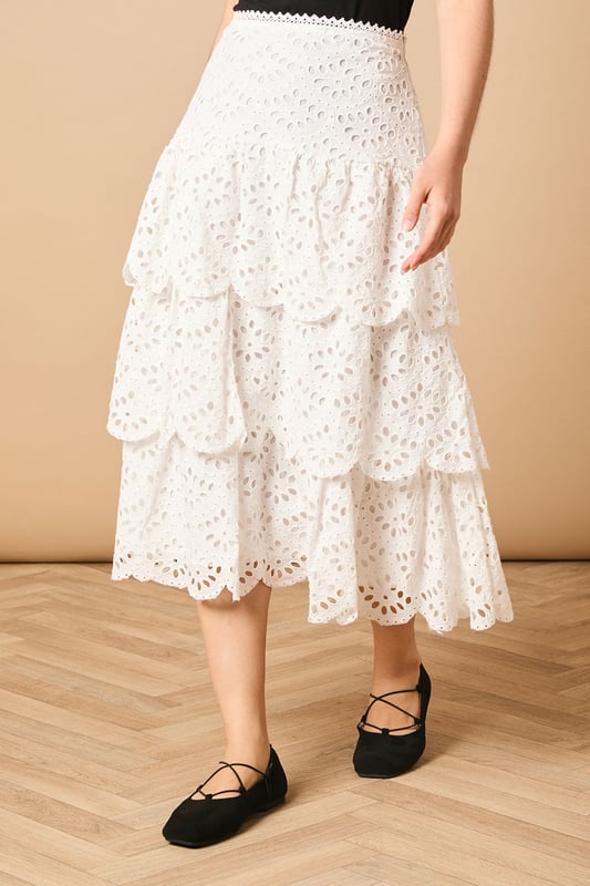 Intricate broderie anglaise detailing with floral eyelet pattern throughout
        Elegant tiered design creates beautiful movement and dimension
        Midi length falls gracefully below the knee for a feminine silhouette
        Scalloped hem adds a delicate finishing touch to each tier
        High-waisted fit accentuates the natural waistline
    
    This charming broderie tiered midi skirt from Oasis combines timeless femininity with contemporary styling. The delicate eyelet pattern creates a romantic texture that catches the light beautifully as you move, while the tiered construction adds playful volume and flow. Style with a denim waistcoat as shown for a balanced casual look, or pair with a fitted blouse for garden parties and family gatherings. The versatile midi length works wonderfully with both ankle boots for cooler days or flat sandals when the temperature rises. This skirt transitions effortlessly from daytime outings to casual evening events - simply switch your accessories to refresh your look. The high-waisted design flatters your figure whilst providing comfort for all-day wear.