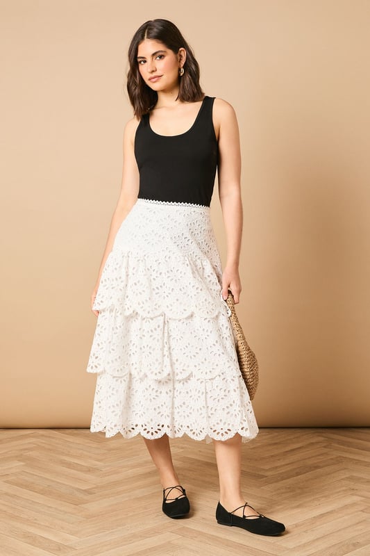 Intricate broderie anglaise detailing with floral eyelet pattern throughout
        Elegant tiered design creates beautiful movement and dimension
        Midi length falls gracefully below the knee for a feminine silhouette
        Scalloped hem adds a delicate finishing touch to each tier
        High-waisted fit accentuates the natural waistline
    
    This charming broderie tiered midi skirt from Oasis combines timeless femininity with contemporary styling. The delicate eyelet pattern creates a romantic texture that catches the light beautifully as you move, while the tiered construction adds playful volume and flow. Style with a denim waistcoat as shown for a balanced casual look, or pair with a fitted blouse for garden parties and family gatherings. The versatile midi length works wonderfully with both ankle boots for cooler days or flat sandals when the temperature rises. This skirt transitions effortlessly from daytime outings to casual evening events - simply switch your accessories to refresh your look. The high-waisted design flatters your figure whilst providing comfort for all-day wear.