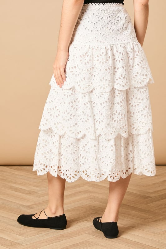 Intricate broderie anglaise detailing with floral eyelet pattern throughout
        Elegant tiered design creates beautiful movement and dimension
        Midi length falls gracefully below the knee for a feminine silhouette
        Scalloped hem adds a delicate finishing touch to each tier
        High-waisted fit accentuates the natural waistline
    
    This charming broderie tiered midi skirt from Oasis combines timeless femininity with contemporary styling. The delicate eyelet pattern creates a romantic texture that catches the light beautifully as you move, while the tiered construction adds playful volume and flow. Style with a denim waistcoat as shown for a balanced casual look, or pair with a fitted blouse for garden parties and family gatherings. The versatile midi length works wonderfully with both ankle boots for cooler days or flat sandals when the temperature rises. This skirt transitions effortlessly from daytime outings to casual evening events - simply switch your accessories to refresh your look. The high-waisted design flatters your figure whilst providing comfort for all-day wear.