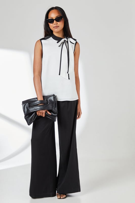 Sleeveless satin top with striking contrast trim along the neckline and armholes
        Elegant tie-neck detail creates a sophisticated bow at the collar
        High neckline offers a refined silhouette perfect for formal settings
        Clean, straight-cut hemline for a polished finish
        Smooth woven fabric with a subtle lustre for an elegant appearance
    
    This Principles sleeveless top combines timeless elegance with contemporary design through its distinctive contrast detailing. The sophisticated tie-neck feature allows for versatile styling-wear it neatly tied for formal occasions or slightly loosened for a more relaxed interpretation. Pair with wide-leg trousers as shown for a chic monochromatic ensemble that transitions seamlessly from office to evening events. For formal occasions, style with a tailored blazer, statement earrings and court shoes. Alternatively, create a smart-casual look by teaming with slim-fit trousers and pointed flats. The clean lines and classic contrast colouring make this top an excellent foundation piece for multiple outfits, whether attending a wedding reception, business meeting, or sophisticated dinner engagement.