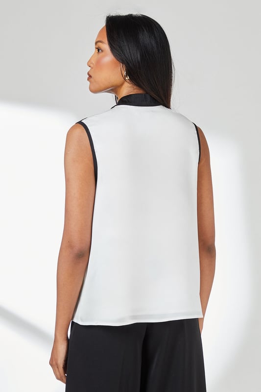Sleeveless satin top with striking contrast trim along the neckline and armholes
        Elegant tie-neck detail creates a sophisticated bow at the collar
        High neckline offers a refined silhouette perfect for formal settings
        Clean, straight-cut hemline for a polished finish
        Smooth woven fabric with a subtle lustre for an elegant appearance
    
    This Principles sleeveless top combines timeless elegance with contemporary design through its distinctive contrast detailing. The sophisticated tie-neck feature allows for versatile styling-wear it neatly tied for formal occasions or slightly loosened for a more relaxed interpretation. Pair with wide-leg trousers as shown for a chic monochromatic ensemble that transitions seamlessly from office to evening events. For formal occasions, style with a tailored blazer, statement earrings and court shoes. Alternatively, create a smart-casual look by teaming with slim-fit trousers and pointed flats. The clean lines and classic contrast colouring make this top an excellent foundation piece for multiple outfits, whether attending a wedding reception, business meeting, or sophisticated dinner engagement.