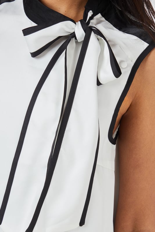 Sleeveless satin top with striking contrast trim along the neckline and armholes
        Elegant tie-neck detail creates a sophisticated bow at the collar
        High neckline offers a refined silhouette perfect for formal settings
        Clean, straight-cut hemline for a polished finish
        Smooth woven fabric with a subtle lustre for an elegant appearance
    
    This Principles sleeveless top combines timeless elegance with contemporary design through its distinctive contrast detailing. The sophisticated tie-neck feature allows for versatile styling-wear it neatly tied for formal occasions or slightly loosened for a more relaxed interpretation. Pair with wide-leg trousers as shown for a chic monochromatic ensemble that transitions seamlessly from office to evening events. For formal occasions, style with a tailored blazer, statement earrings and court shoes. Alternatively, create a smart-casual look by teaming with slim-fit trousers and pointed flats. The clean lines and classic contrast colouring make this top an excellent foundation piece for multiple outfits, whether attending a wedding reception, business meeting, or sophisticated dinner engagement.