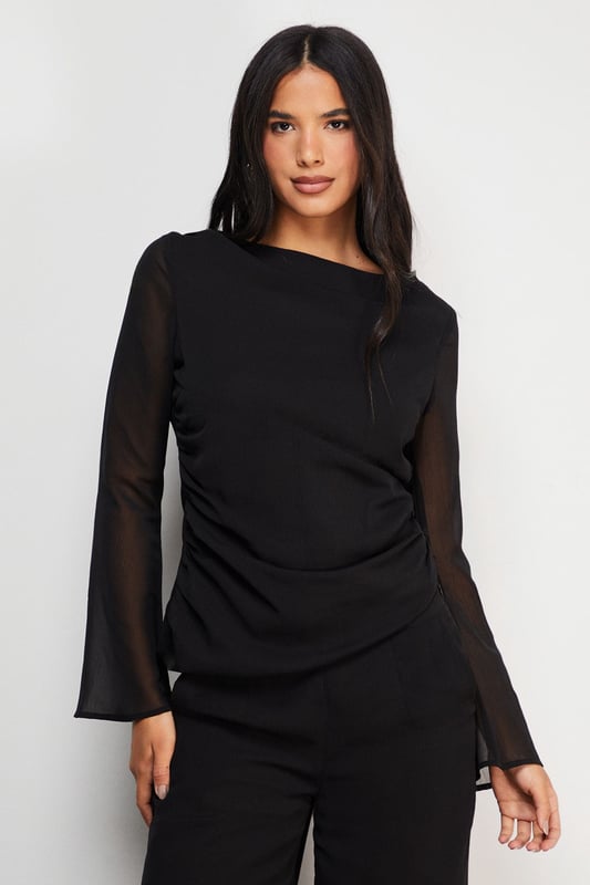 Elegant chiffon top featuring a sophisticated asymmetric design
        Flattering gathered waist detail creates a feminine silhouette
        Sheer long sleeves add a touch of subtle allure
        Versatile boat neckline frames the dcolletage beautifully
        Fully lined body ensures comfort and proper coverage
    
    This Warehouse chiffon top combines contemporary design with effortless wearability. The asymmetric gathering at the waist creates a flattering drape that complements your natural shape, whilst the sheer sleeves add a delicate contrast to the lined body. Style with wide-leg trousers as shown for a sophisticated daytime look, or dress up with tailored cigarette trousers and statement earrings for evening drinks. The versatile design transitions seamlessly from office to weekend brunch, making it a wardrobe essential for the modern British woman. For casual family gatherings, pair with your favourite denim and ballet flats, or dress it up with a sleek blazer and heeled boots for dinner dates. Machine washable for practical everyday wear.