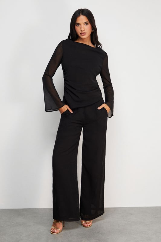 Elegant chiffon top featuring a sophisticated asymmetric design
        Flattering gathered waist detail creates a feminine silhouette
        Sheer long sleeves add a touch of subtle allure
        Versatile boat neckline frames the dcolletage beautifully
        Fully lined body ensures comfort and proper coverage
    
    This Warehouse chiffon top combines contemporary design with effortless wearability. The asymmetric gathering at the waist creates a flattering drape that complements your natural shape, whilst the sheer sleeves add a delicate contrast to the lined body. Style with wide-leg trousers as shown for a sophisticated daytime look, or dress up with tailored cigarette trousers and statement earrings for evening drinks. The versatile design transitions seamlessly from office to weekend brunch, making it a wardrobe essential for the modern British woman. For casual family gatherings, pair with your favourite denim and ballet flats, or dress it up with a sleek blazer and heeled boots for dinner dates. Machine washable for practical everyday wear.