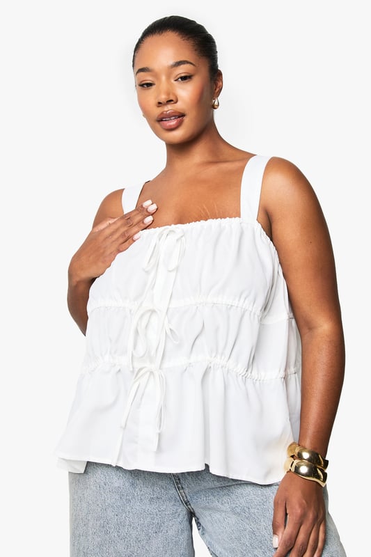 Wide shoulder straps for comfortable all-day wear
        Tiered design with ruched detailing for added texture and dimension
        Front tie detail with delicate drawstrings for adjustable styling
        Relaxed peplum hem creating a flattering silhouette
        Square neckline offering a contemporary, feminine touch
    
    This charming cami top combines comfort with effortless style for your casual wardrobe. The tiered design creates visual interest whilst the ruched detailing adds a touch of playfulness to your look. Style with light-wash denim jeans as shown for a relaxed daytime ensemble, or pair with tailored trousers for a smart-casual finish. The adjustable tie details allow you to customise the fit to your preference, making it ideal for family gatherings or weekend brunches. Accessorise with gold-toned jewellery to enhance the laid-back yet put-together aesthetic. Perfect for the warmer months, this versatile Boohoo piece transitions seamlessly from day to evening with a simple change of accessories - swap your trainers for espadrilles and add a crossbody bag for an effortless summer look.