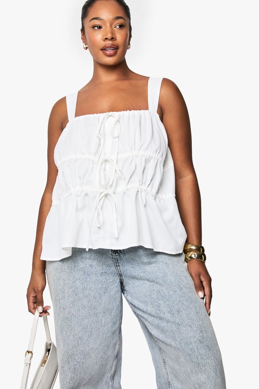 Wide shoulder straps for comfortable all-day wear
        Tiered design with ruched detailing for added texture and dimension
        Front tie detail with delicate drawstrings for adjustable styling
        Relaxed peplum hem creating a flattering silhouette
        Square neckline offering a contemporary, feminine touch
    
    This charming cami top combines comfort with effortless style for your casual wardrobe. The tiered design creates visual interest whilst the ruched detailing adds a touch of playfulness to your look. Style with light-wash denim jeans as shown for a relaxed daytime ensemble, or pair with tailored trousers for a smart-casual finish. The adjustable tie details allow you to customise the fit to your preference, making it ideal for family gatherings or weekend brunches. Accessorise with gold-toned jewellery to enhance the laid-back yet put-together aesthetic. Perfect for the warmer months, this versatile Boohoo piece transitions seamlessly from day to evening with a simple change of accessories - swap your trainers for espadrilles and add a crossbody bag for an effortless summer look.