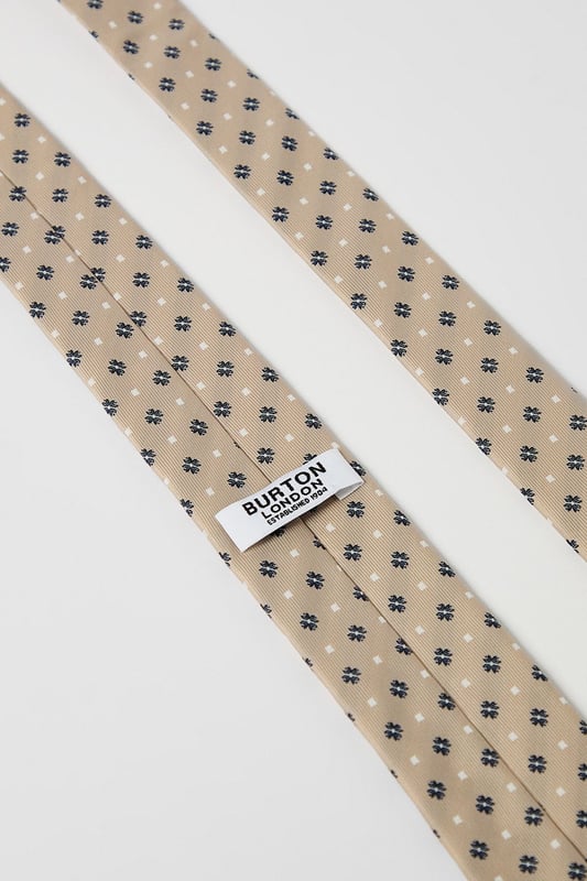 Classic foulard pattern tie with geometric motif for timeless appeal
        Standard width design suitable for both modern and traditional suit styles
        Smooth finish for comfortable all-day wear
        Neat pointed tip with branded lining detail
        Authentic Burton label for quality assurance
    
    This sophisticated foulard tie brings understated elegance to any outfit. The repeating geometric pattern creates visual interest without overwhelming your look, making it perfect for various occasions. Pair with a crisp white shirt and navy blazer for family gatherings or weekend brunches. For casual office days, match with a light blue Oxford shirt and chinos. The versatile design works brilliantly with both plain and subtly patterned shirts, allowing you to create numerous combinations from your existing wardrobe. This Burton tie offers the perfect balance between formal and relaxed styling - ideal for the man who appreciates classic accessories that transition effortlessly from day to evening events. Whether you're heading to the pub with friends or attending a casual wedding, this tie adds a refined finishing touch.