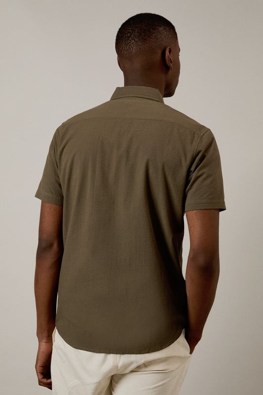Textured seersucker fabric adds subtle dimension and visual interest
        Classic short sleeve design with traditional collar for timeless appeal
        Single chest pocket detail for practical functionality
        Button-through front with clean finish for easy styling
        Relaxed cut allows for comfortable movement throughout the day
    
    This seersucker short sleeve shirt from Burton delivers effortless style for the modern man who values both comfort and classic design. The distinctive textured fabric is naturally breathable, making it ideal for warmer days when you need to stay cool yet look put-together. Pair with chino shorts as shown for casual weekend outings or garden gatherings. For a smart-casual look, team with tailored trousers and loafers when heading to the pub with mates or a relaxed family lunch. The versatile nature of this shirt means it works equally well layered over a plain t-shirt or worn alone. Machine washable at 30 degrees, this low-maintenance essential will quickly become a go-to in your warm-weather rotation, offering that perfect balance of relaxed sophistication that Burton is known for.