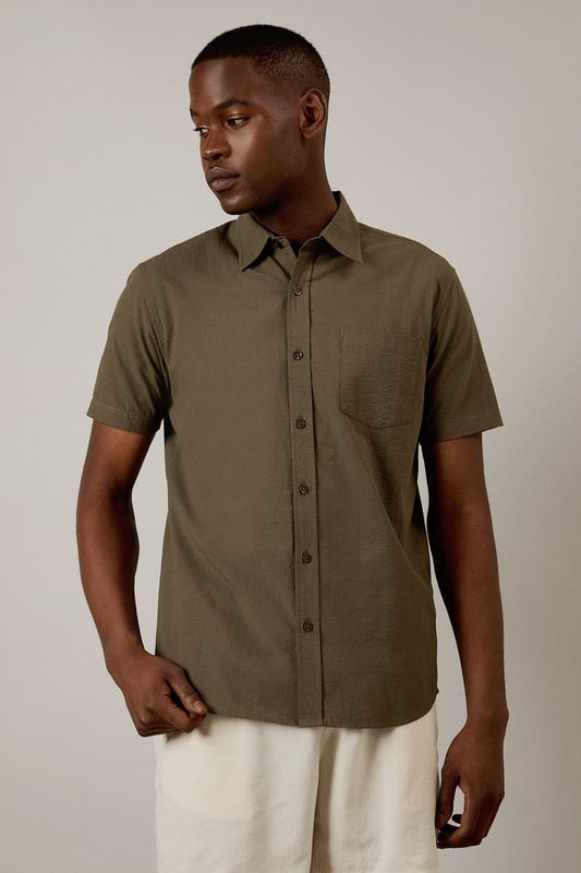 Textured seersucker fabric adds subtle dimension and visual interest
        Classic short sleeve design with traditional collar for timeless appeal
        Single chest pocket detail for practical functionality
        Button-through front with clean finish for easy styling
        Relaxed cut allows for comfortable movement throughout the day
    
    This seersucker short sleeve shirt from Burton delivers effortless style for the modern man who values both comfort and classic design. The distinctive textured fabric is naturally breathable, making it ideal for warmer days when you need to stay cool yet look put-together. Pair with chino shorts as shown for casual weekend outings or garden gatherings. For a smart-casual look, team with tailored trousers and loafers when heading to the pub with mates or a relaxed family lunch. The versatile nature of this shirt means it works equally well layered over a plain t-shirt or worn alone. Machine washable at 30 degrees, this low-maintenance essential will quickly become a go-to in your warm-weather rotation, offering that perfect balance of relaxed sophistication that Burton is known for.