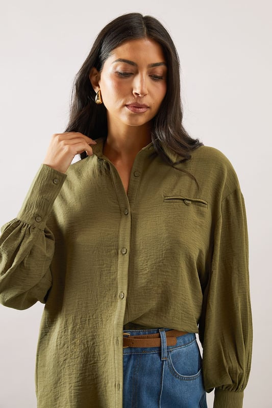 Relaxed fit collared shirt with elegant chest pocket detail
        Voluminous balloon sleeves with fitted cuffs for a feminine silhouette
        Soft woven fabric with slight stretch for all-day comfort
        Classic button-through front with sophisticated collar design
        Curved hem perfect for both tucked or untucked styling options
    
    This versatile Wallis shirt combines sophistication with everyday comfort. The relaxed silhouette drapes beautifully over the body while the distinctive pocket detail adds a touch of refinement. Style it as shown with wide-leg denim trousers and trainers for a polished daytime look, or tuck the front into tailored trousers for family gatherings. The balloon sleeves create a contemporary shape that transitions effortlessly from office to weekend brunch. For cooler days, layer under a lightweight cardigan or pair with your favourite jeans and ankle boots. The collared neckline frames the face beautifully, making this shirt an essential addition to your daywear collection - perfect for those occasions when you want to feel put-together yet comfortable.
