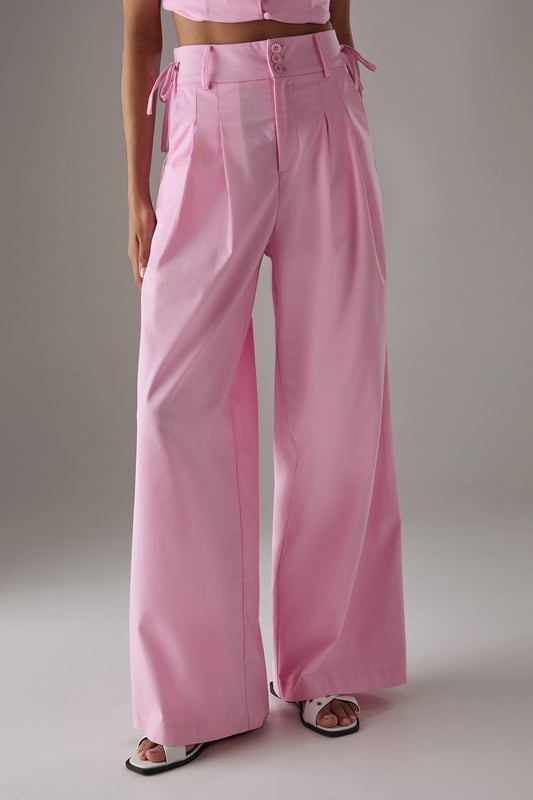 Tailored wide-leg silhouette with a dramatic flowing drape
        Elegant front pleats for added structure and dimension
        Distinctive side tie detail with decorative buttons for a feminine touch
        High-rise waistband designed to flatter the natural waistline
        Linen blend fabric offering breathability and a natural textured finish
    
    These statement trousers from Warehouse combine sophistication with contemporary flair. The wide-leg design creates a striking silhouette that moves beautifully with every step, whilst the tailored pleats add structure and refinement. Style with a simple white tee and flat sandals for effortless daytime chic, or pair with the matching waistcoat for a coordinated ensemble that's perfect for summer gatherings. The versatile design transitions seamlessly from casual brunches to family celebrations - simply swap your trainers for leather slides and add delicate jewellery to enhance the look. The linen blend fabric ensures these trousers remain comfortable throughout the day, making them an essential addition to your warm-weather wardrobe.