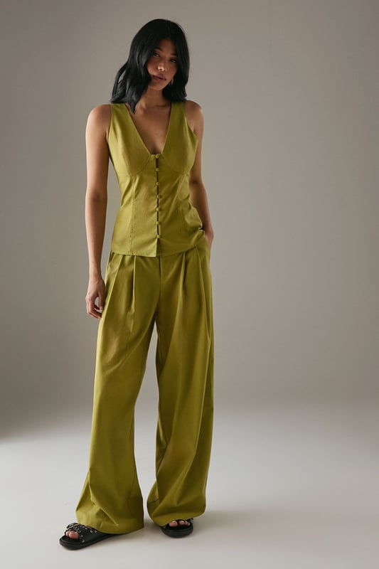 Tailored wide-leg silhouette with a dramatic flowing drape
        Elegant front pleats for added structure and dimension
        Distinctive side tie detail with decorative buttons for a feminine touch
        High-rise waistband designed to flatter the natural waistline
        Linen blend fabric offering breathability and a natural textured finish
    
    These statement trousers from Warehouse combine sophistication with contemporary flair. The wide-leg design creates a striking silhouette that moves beautifully with every step, whilst the tailored pleats add structure and refinement. Style with a simple white tee and flat sandals for effortless daytime chic, or pair with the matching waistcoat for a coordinated ensemble that's perfect for summer gatherings. The versatile design transitions seamlessly from casual brunches to family celebrations - simply swap your trainers for leather slides and add delicate jewellery to enhance the look. The linen blend fabric ensures these trousers remain comfortable throughout the day, making them an essential addition to your warm-weather wardrobe.