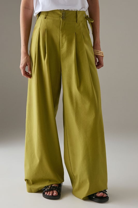 Tailored wide-leg silhouette with a dramatic flowing drape
        Elegant front pleats for added structure and dimension
        Distinctive side tie detail with decorative buttons for a feminine touch
        High-rise waistband designed to flatter the natural waistline
        Linen blend fabric offering breathability and a natural textured finish
    
    These statement trousers from Warehouse combine sophistication with contemporary flair. The wide-leg design creates a striking silhouette that moves beautifully with every step, whilst the tailored pleats add structure and refinement. Style with a simple white tee and flat sandals for effortless daytime chic, or pair with the matching waistcoat for a coordinated ensemble that's perfect for summer gatherings. The versatile design transitions seamlessly from casual brunches to family celebrations - simply swap your trainers for leather slides and add delicate jewellery to enhance the look. The linen blend fabric ensures these trousers remain comfortable throughout the day, making them an essential addition to your warm-weather wardrobe.