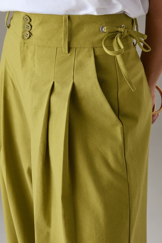 Tailored wide-leg silhouette with a dramatic flowing drape
        Elegant front pleats for added structure and dimension
        Distinctive side tie detail with decorative buttons for a feminine touch
        High-rise waistband designed to flatter the natural waistline
        Linen blend fabric offering breathability and a natural textured finish
    
    These statement trousers from Warehouse combine sophistication with contemporary flair. The wide-leg design creates a striking silhouette that moves beautifully with every step, whilst the tailored pleats add structure and refinement. Style with a simple white tee and flat sandals for effortless daytime chic, or pair with the matching waistcoat for a coordinated ensemble that's perfect for summer gatherings. The versatile design transitions seamlessly from casual brunches to family celebrations - simply swap your trainers for leather slides and add delicate jewellery to enhance the look. The linen blend fabric ensures these trousers remain comfortable throughout the day, making them an essential addition to your warm-weather wardrobe.