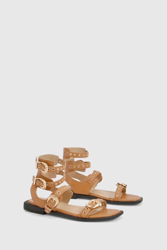 Striking gladiator design with distinctive Western-style buckle detailing
        Multiple adjustable straps for a secure and customisable fit
        Flat sole with comfortable 0-2cm heel height for all-day wear
        Open toe silhouette with sleek ankle cuff for added support
        Durable PU construction with gold-tone hardware accents
    
    Make a statement this season with these eye-catching gladiator sandals featuring Western-inspired buckles. The multi-strap design creates a bold look that commands attention whilst remaining surprisingly versatile for your summer wardrobe. Style with frayed denim shorts and an oversized linen shirt for casual daytime outings, or pair with a flowing midi dress for garden parties and family gatherings. The flat design ensures comfort for extended wear, whether you're strolling through city streets or attending a casual festival. These sandals work brilliantly with both neutral and vibrant outfits, making them a practical yet fashionable choice for your holiday suitcase. As shown in the images, they complement a minimalist handbag perfectly for an effortlessly coordinated look that transitions seamlessly from day to evening casual events.