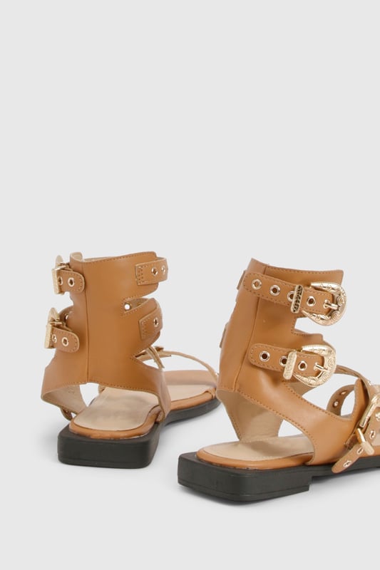 Striking gladiator design with distinctive Western-style buckle detailing
        Multiple adjustable straps for a secure and customisable fit
        Flat sole with comfortable 0-2cm heel height for all-day wear
        Open toe silhouette with sleek ankle cuff for added support
        Durable PU construction with gold-tone hardware accents
    
    Make a statement this season with these eye-catching gladiator sandals featuring Western-inspired buckles. The multi-strap design creates a bold look that commands attention whilst remaining surprisingly versatile for your summer wardrobe. Style with frayed denim shorts and an oversized linen shirt for casual daytime outings, or pair with a flowing midi dress for garden parties and family gatherings. The flat design ensures comfort for extended wear, whether you're strolling through city streets or attending a casual festival. These sandals work brilliantly with both neutral and vibrant outfits, making them a practical yet fashionable choice for your holiday suitcase. As shown in the images, they complement a minimalist handbag perfectly for an effortlessly coordinated look that transitions seamlessly from day to evening casual events.
