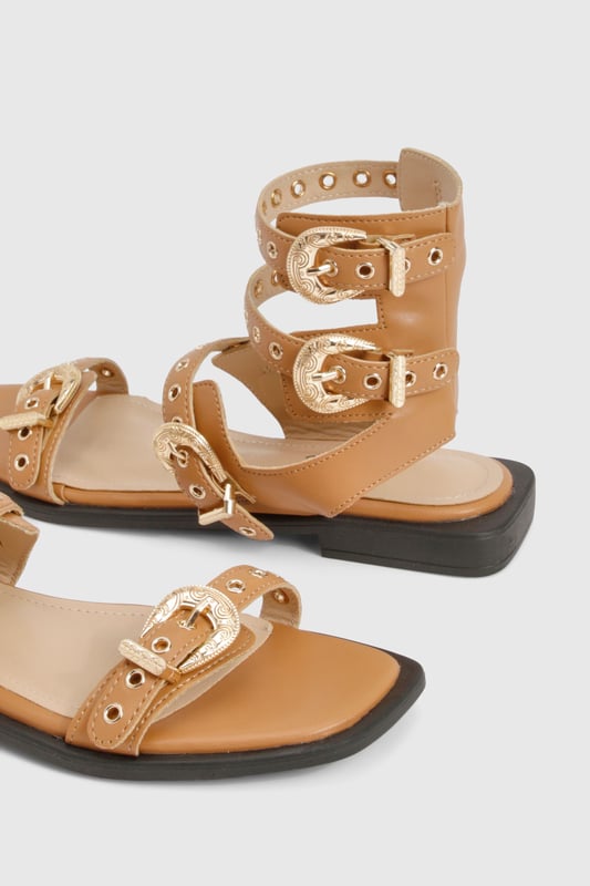 Striking gladiator design with distinctive Western-style buckle detailing
        Multiple adjustable straps for a secure and customisable fit
        Flat sole with comfortable 0-2cm heel height for all-day wear
        Open toe silhouette with sleek ankle cuff for added support
        Durable PU construction with gold-tone hardware accents
    
    Make a statement this season with these eye-catching gladiator sandals featuring Western-inspired buckles. The multi-strap design creates a bold look that commands attention whilst remaining surprisingly versatile for your summer wardrobe. Style with frayed denim shorts and an oversized linen shirt for casual daytime outings, or pair with a flowing midi dress for garden parties and family gatherings. The flat design ensures comfort for extended wear, whether you're strolling through city streets or attending a casual festival. These sandals work brilliantly with both neutral and vibrant outfits, making them a practical yet fashionable choice for your holiday suitcase. As shown in the images, they complement a minimalist handbag perfectly for an effortlessly coordinated look that transitions seamlessly from day to evening casual events.