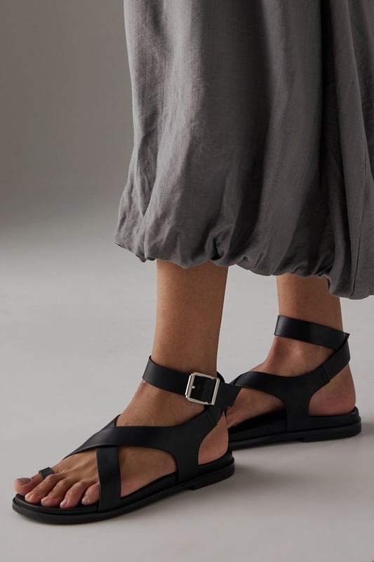 Stylish toe loop design for a secure and comfortable fit
        Adjustable ankle strap with metal buckle fastening for a customised fit
        Flat footbed with cushioned insole for all-day comfort
        Cross-over straps create an elegant silhouette
        Durable outsole with subtle tread for reliable grip
    
    The Faith Mannie sandals combine contemporary design with everyday practicality. The distinctive toe loop and cross-over straps create a modern silhouette that pairs beautifully with flowing dresses, as shown by our model, or relaxed linen trousers for effortless summer style. With their flat heel measuring under 2cm, these sandals offer the perfect balance of comfort and sophistication for long summer days. The adjustable ankle strap ensures a secure fit whilst adding a refined detail to this casual footwear essential. Ideal for family gatherings, weekend brunches or holiday strolls, these versatile sandals will quickly become your warm-weather staple. Their faux leather finish gives them a polished appearance that transitions seamlessly from daytime casual to relaxed evening occasions.