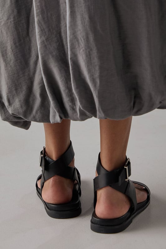 Stylish toe loop design for a secure and comfortable fit
        Adjustable ankle strap with metal buckle fastening for a customised fit
        Flat footbed with cushioned insole for all-day comfort
        Cross-over straps create an elegant silhouette
        Durable outsole with subtle tread for reliable grip
    
    The Faith Mannie sandals combine contemporary design with everyday practicality. The distinctive toe loop and cross-over straps create a modern silhouette that pairs beautifully with flowing dresses, as shown by our model, or relaxed linen trousers for effortless summer style. With their flat heel measuring under 2cm, these sandals offer the perfect balance of comfort and sophistication for long summer days. The adjustable ankle strap ensures a secure fit whilst adding a refined detail to this casual footwear essential. Ideal for family gatherings, weekend brunches or holiday strolls, these versatile sandals will quickly become your warm-weather staple. Their faux leather finish gives them a polished appearance that transitions seamlessly from daytime casual to relaxed evening occasions.
