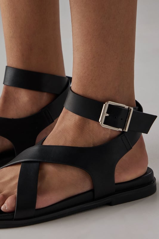 Stylish toe loop design for a secure and comfortable fit
        Adjustable ankle strap with metal buckle fastening for a customised fit
        Flat footbed with cushioned insole for all-day comfort
        Cross-over straps create an elegant silhouette
        Durable outsole with subtle tread for reliable grip
    
    The Faith Mannie sandals combine contemporary design with everyday practicality. The distinctive toe loop and cross-over straps create a modern silhouette that pairs beautifully with flowing dresses, as shown by our model, or relaxed linen trousers for effortless summer style. With their flat heel measuring under 2cm, these sandals offer the perfect balance of comfort and sophistication for long summer days. The adjustable ankle strap ensures a secure fit whilst adding a refined detail to this casual footwear essential. Ideal for family gatherings, weekend brunches or holiday strolls, these versatile sandals will quickly become your warm-weather staple. Their faux leather finish gives them a polished appearance that transitions seamlessly from daytime casual to relaxed evening occasions.