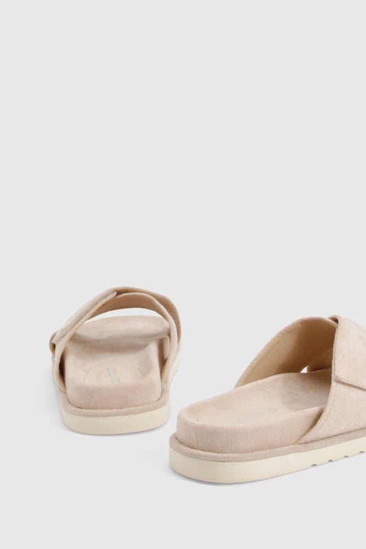 Distinctive cross strap design for a contemporary twist on classic footbed sliders
        Cushioned footbed providing all-day comfort for casual wear
        Flat heel measuring between 0-2cm, perfect for effortless walking
        Textured sole offering reliable grip on various surfaces
        Faux suede finish adding a touch of sophistication to a casual staple
    
    These cross strap footbed sliders combine style and practicality for your everyday wardrobe. The minimalist design features soft faux suede straps that gently hug your feet while the cushioned footbed ensures comfort with every step. Pair them with frayed hem denim shorts and an oversized linen shirt for a relaxed weekend brunch, or style with a flowing maxi dress for garden parties and seaside strolls. Their versatility extends to poolside lounging, where they make the perfect companion to your favourite swimwear. The neutral aesthetic allows these sliders to complement virtually any casual ensemble, making them an essential addition to your summer rotation. Their durable construction means they'll remain a faithful companion throughout the warmer months, ready to slip on whenever comfort calls.