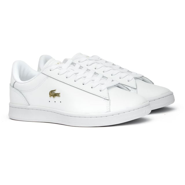 The Lacoste Carnaby Set brings classic court style to your casual collection. These elegant white leather trainers showcase subtle metallic accents that catch the light as you move. With Lacoste's signature branding tastefully placed on the tongue, heel, and quarter, these shoes offer understated luxury. The sturdy rubber cup sole provides reliable traction and durability for everyday wear. Perfect for pairing with anything from tailored trousers to summer dresses.
